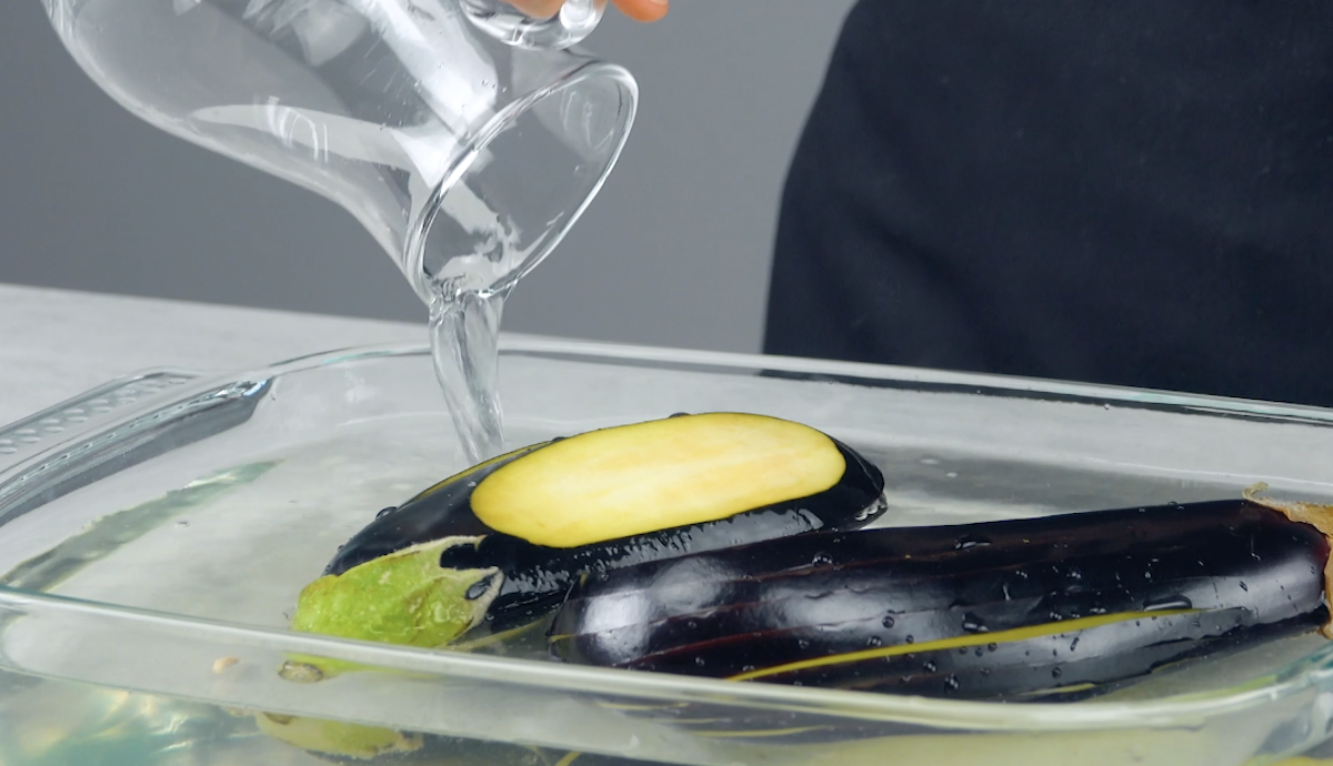 Gefächerte Auberginen in Auflaufform werden mit Wasser übergossen