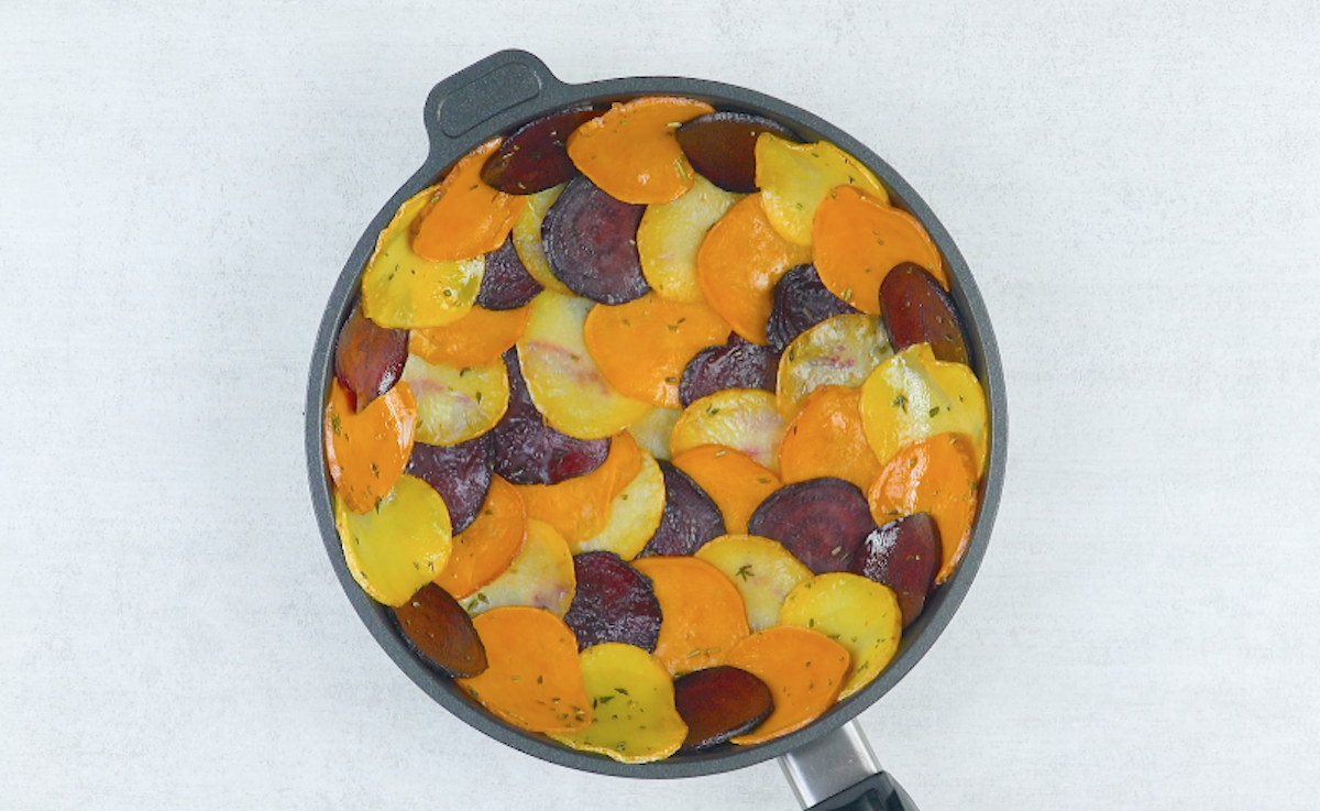 eine Pfanne wird mit dünnen angebratenen Scheiben aus Rote Bete, Kartoffeln und Süßkartoffeln ausgelegt