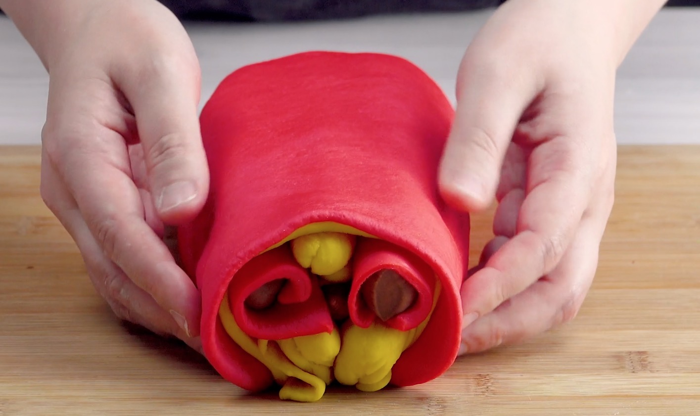 Eine dünn ausgerollte Teigplatte wird um kunstvoll angeordnete rote und gelbe Teigrollen gelegt