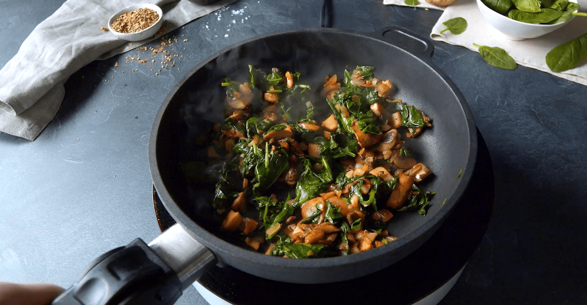 In einer Pfanne wird die aus Champignons, Zwiebeln, Knoblauch und Blattspinat bestehende Füllung für die Arancini angebraten.