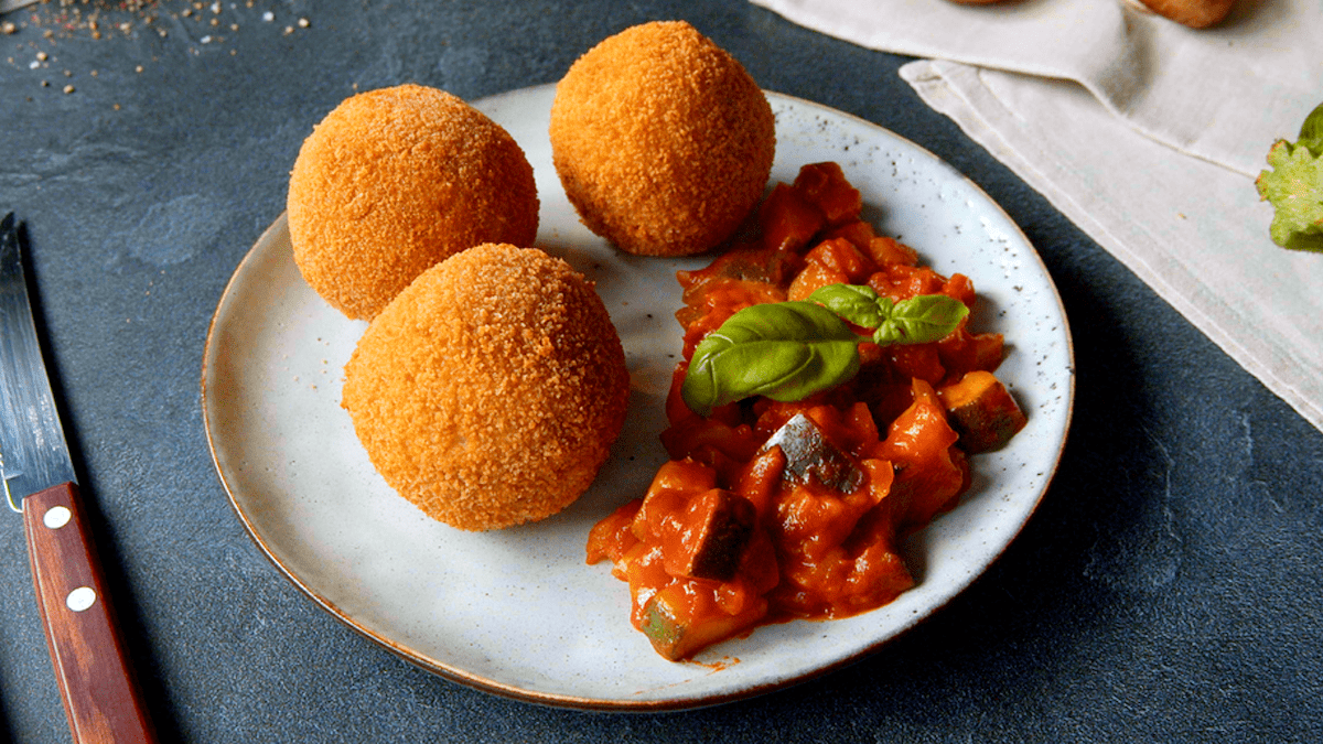 Drei Arancini liegen zusammen mit Tomatensoße servierfertig auf einem weißen Teller.