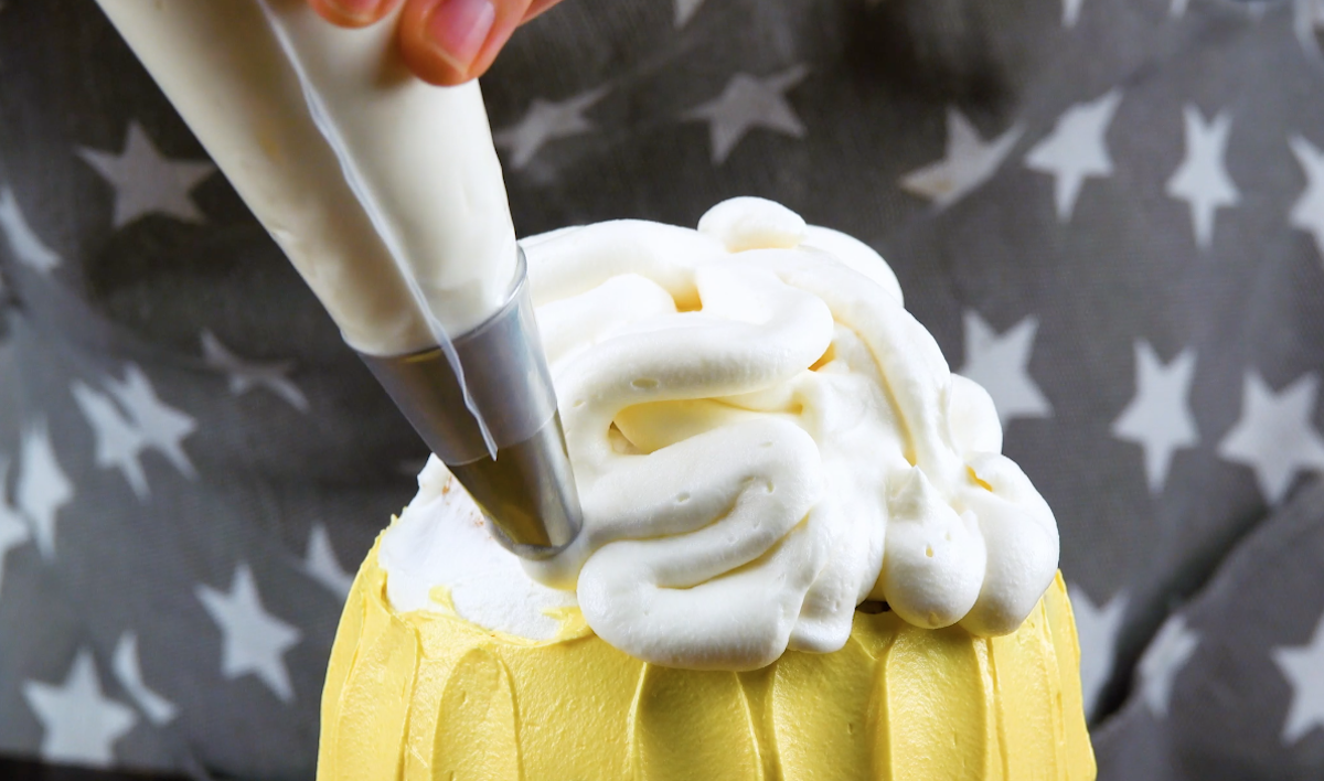 Auf den Kuchen wird weitere weiße Frischkäsecreme mit einem Spritzbeutel gespritzt, sodass sie aussieht wie Schaum