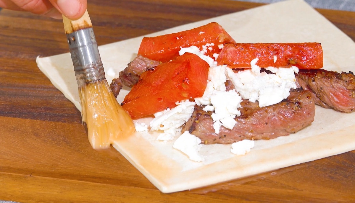 Blätterteig-Quadrat wird mit Melon, Feta udn Rumpsteak belegt und Rand mit Ei bestrichen