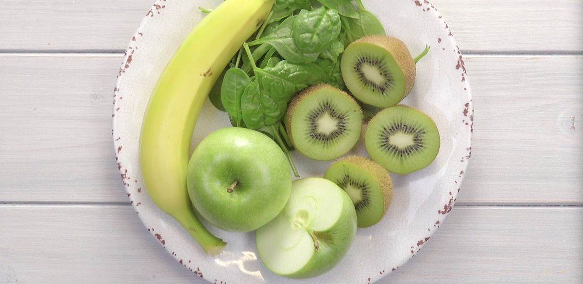 Grüne Äpfel, eine Banane, halbierte Kiwis und eine Handvoll Babyspinat auf einem Teller