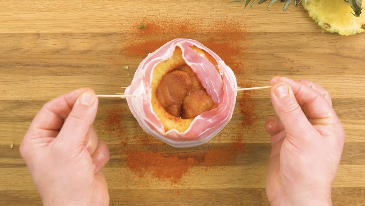 Bacon wird mit Schaschlikspießen an Ananas fixiert