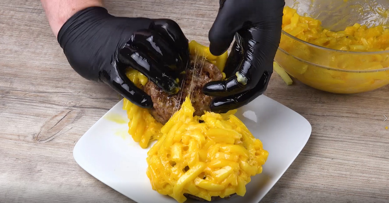 Gebratenes Burger-Patty wird mit Pommes-Käse-Mischung umhüllt