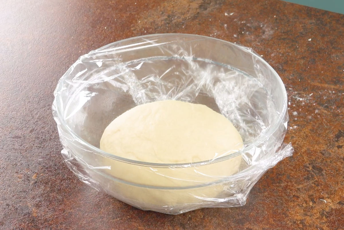 Hefeteig geht in einer Schüssel, die mit Folie zugedeckt ist