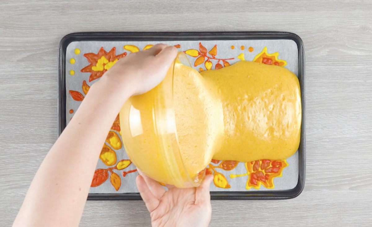 Flüssiger Biskuitteig wird über Blättern auf Backpapier verteilt