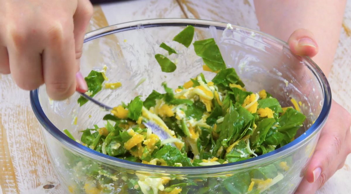 Zerkleinerter Spinat, Frischkäse und geriebener Käse werden in Schüssel miteinander vermengt