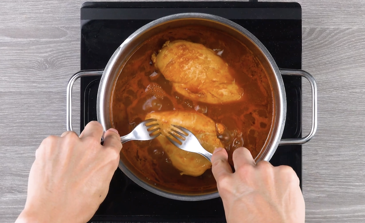 Eine Hühnerbrust wird in einem Topf mit zwei Gabeln auseinander gerupft