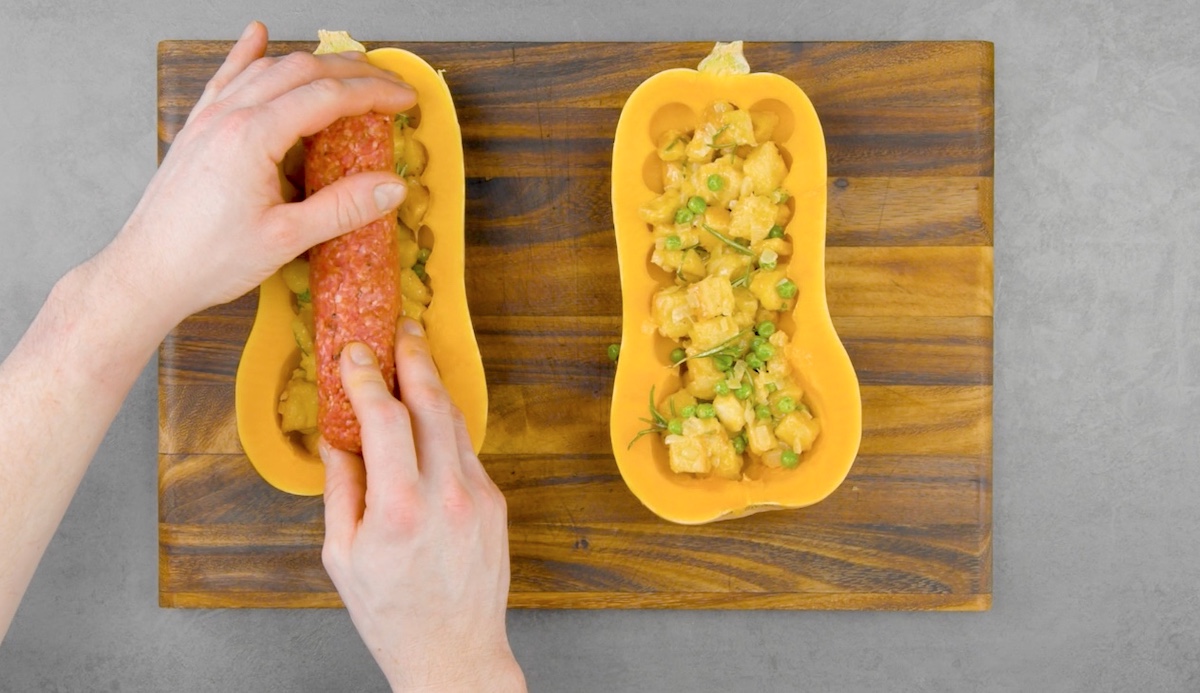 Ein aufgeschnittener Butternusskürbis wird mit Hackfleisch und Gemüse gefüllt