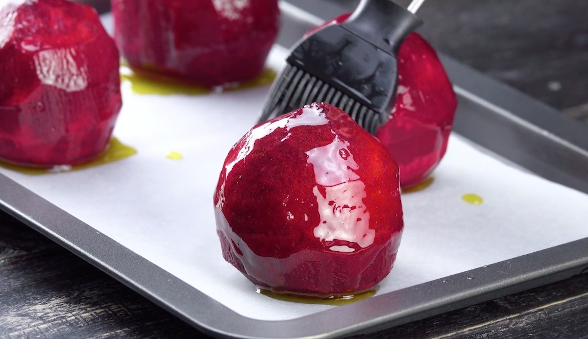 4 geschälte rote Beten auf Backblech werden mit Öl bestrichen