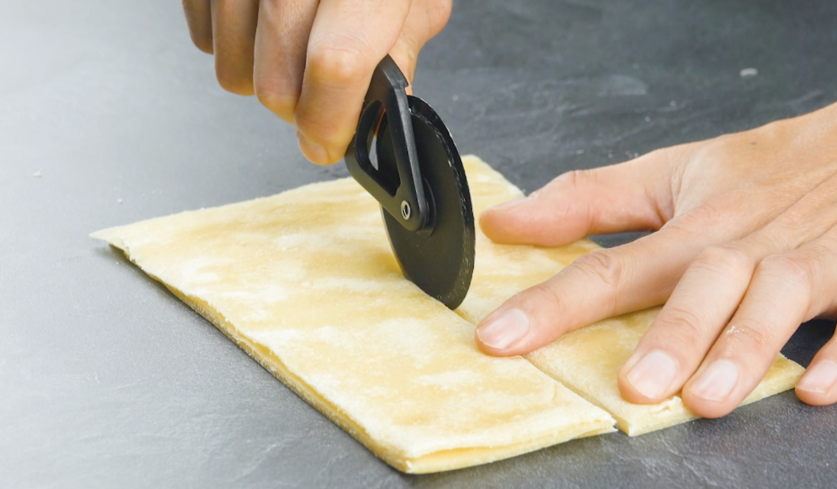 Übereinander gelegter Teig wird erneut mit Pizzaschneider längs in der Mitte halbiert