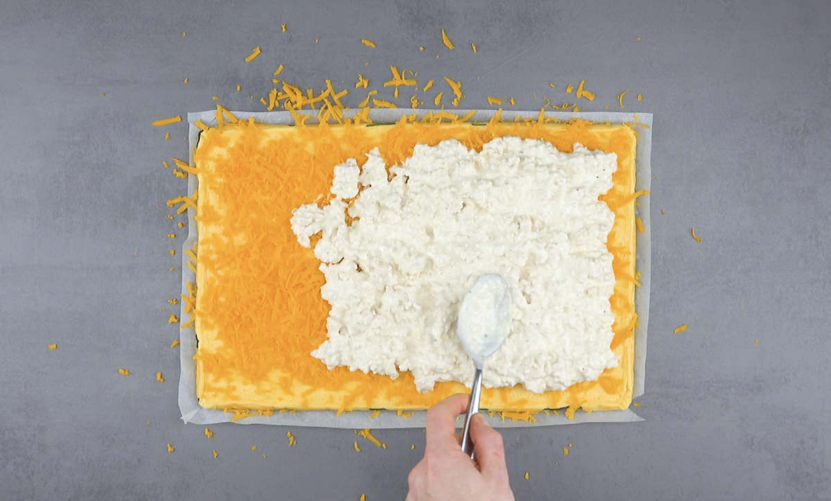 Mit Cheddar bestreutes Zucchini-Omelett wird mit Hähnchen-Masse bestrichen