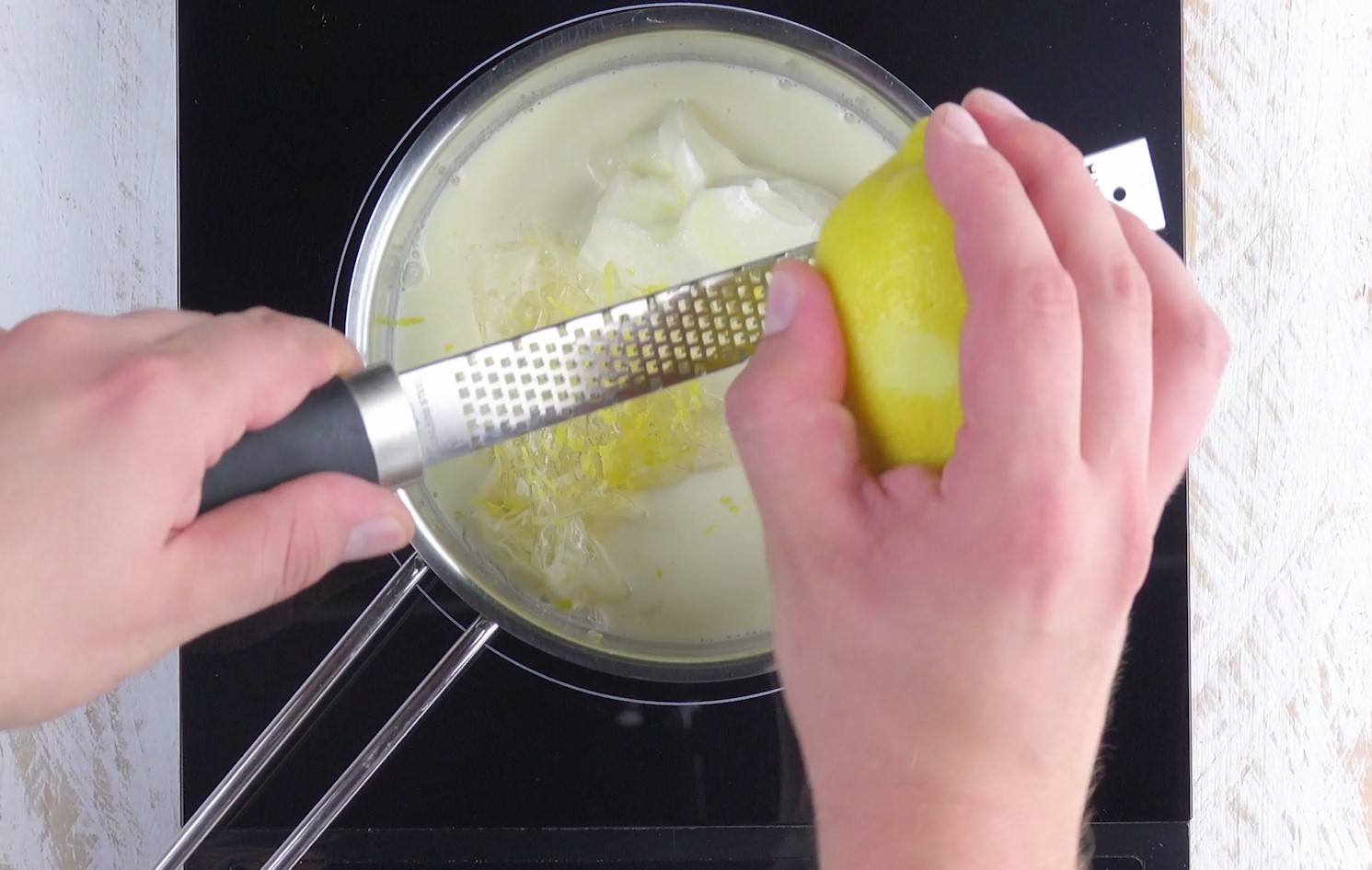 Zitronenschale wird über Topf mit Reibe in Pannacotta gerieben