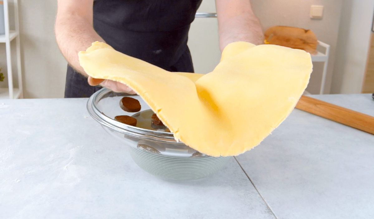 Keksteig wird über einen Pfannendeckel gelegt, in dem in Scheiben geschnittene Schokoganache liegt