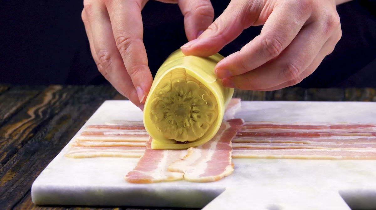 Ein Maiskolben wird in den Käse eingewickelt