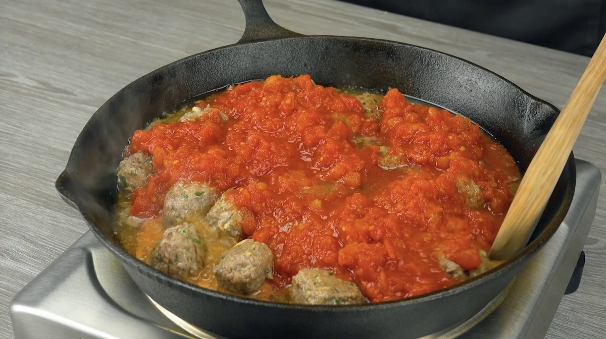Hackbällchen werden mit gehackten Tomaten in Pfanne angebraten
