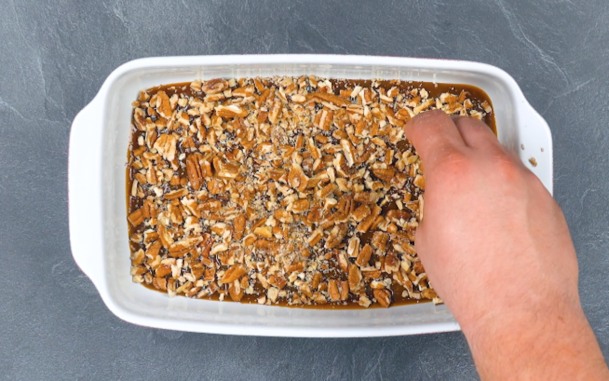 Flüssiges Karamell in Auflaufform wird mit gehackten Pekannüssen bestreut