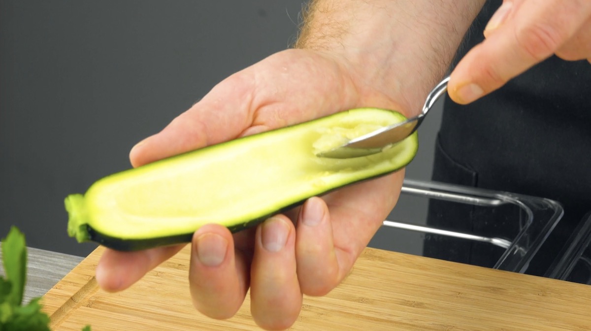 Halbierte Zucchini wird mit Löffel ausgehöhlt