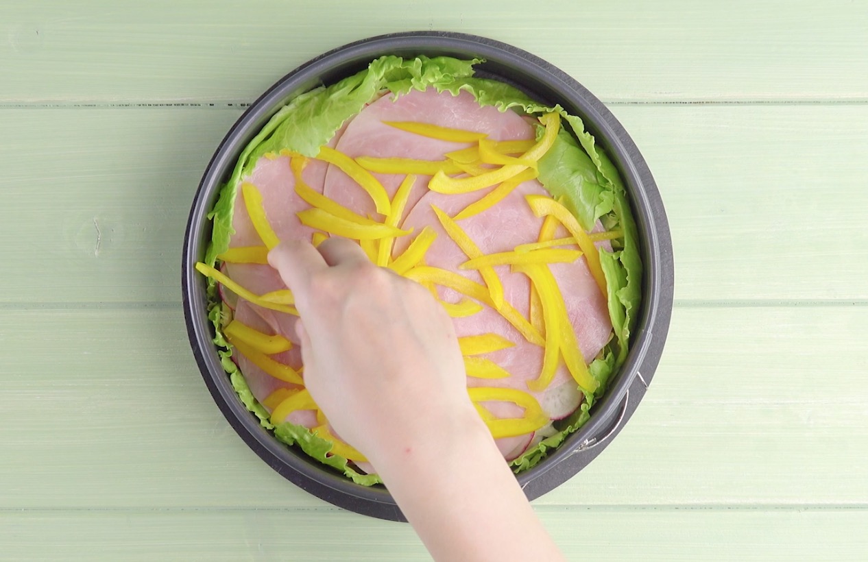 Kochschinkenscheiben und Paprikastreifen werden auf Salatblättern verteilt