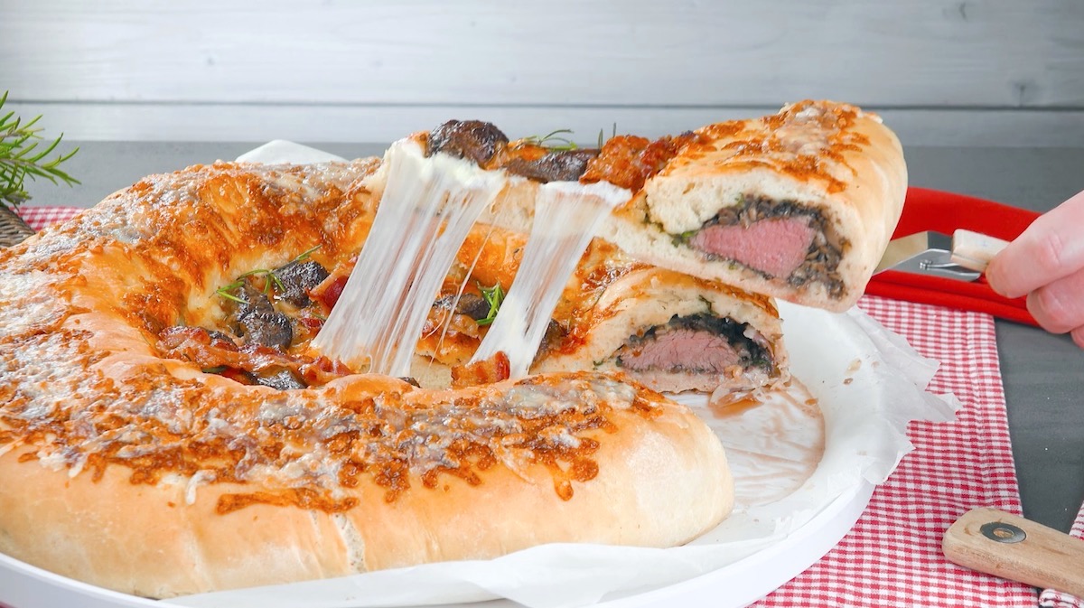 Ein Stück wird aus der Pizza mit Rinderfilet und Champignons im Teig entnommen