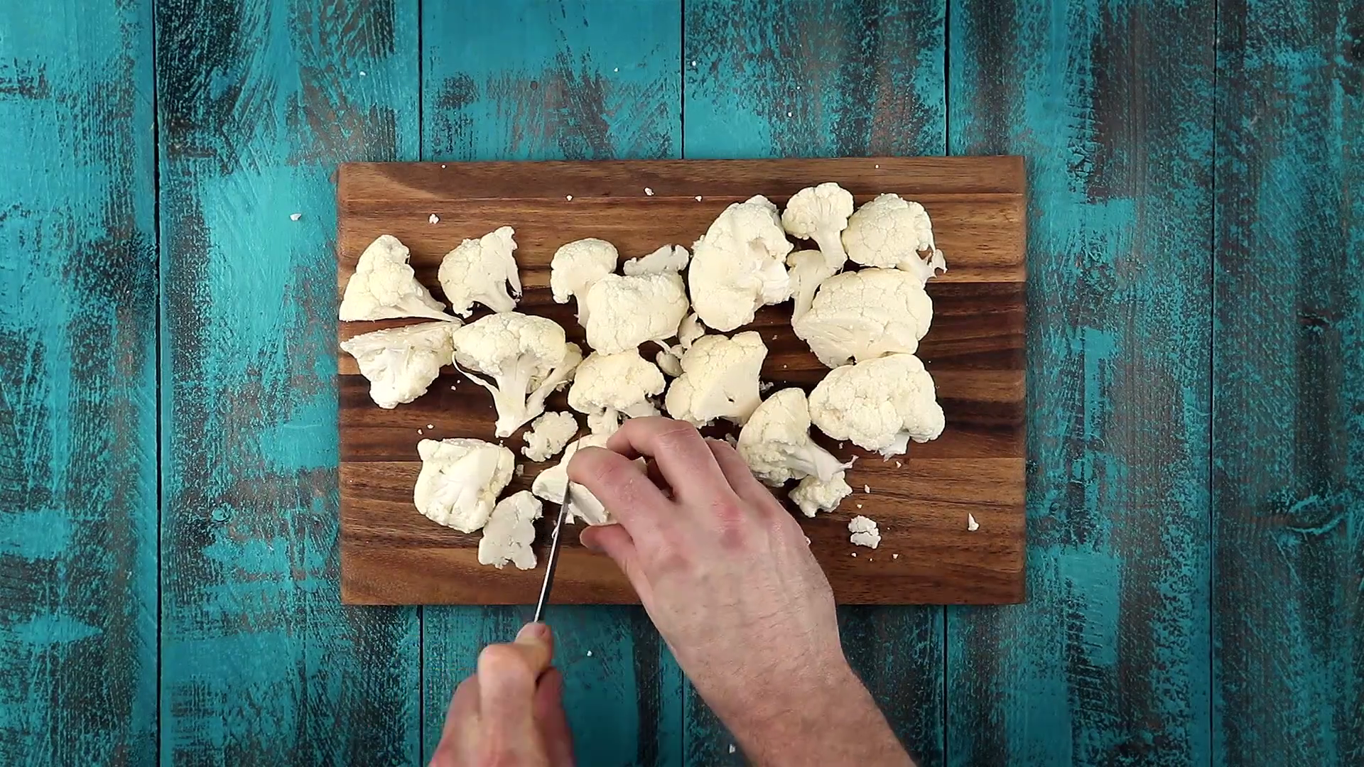 Blumenkohl-Röschen werden mit Messer auf Holzbrett zerkleinert
