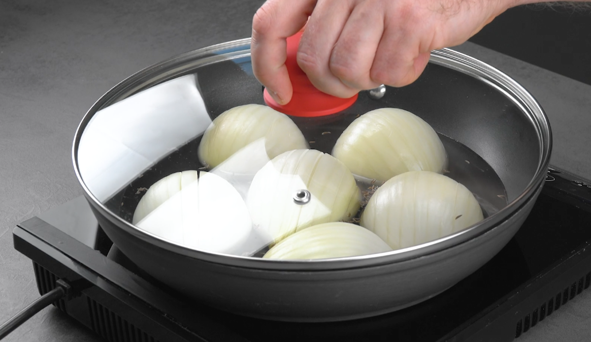 Halbierte Zwiebeln mit Schnittfläche nach unten werden in Pfanne in Gemüsebrühe gegart