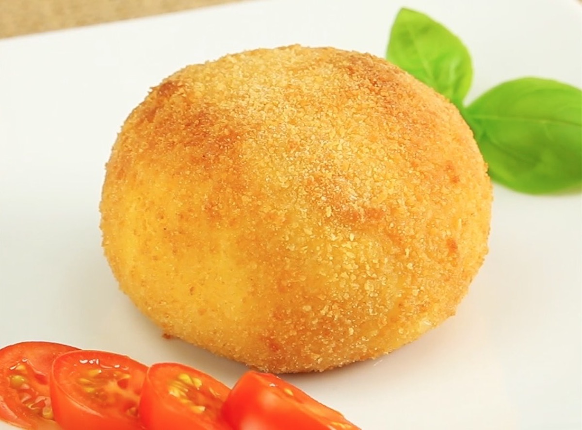 Eine frittierte Mozzarella-Kugel neben Tomatenscheiben und Basilikumblatt