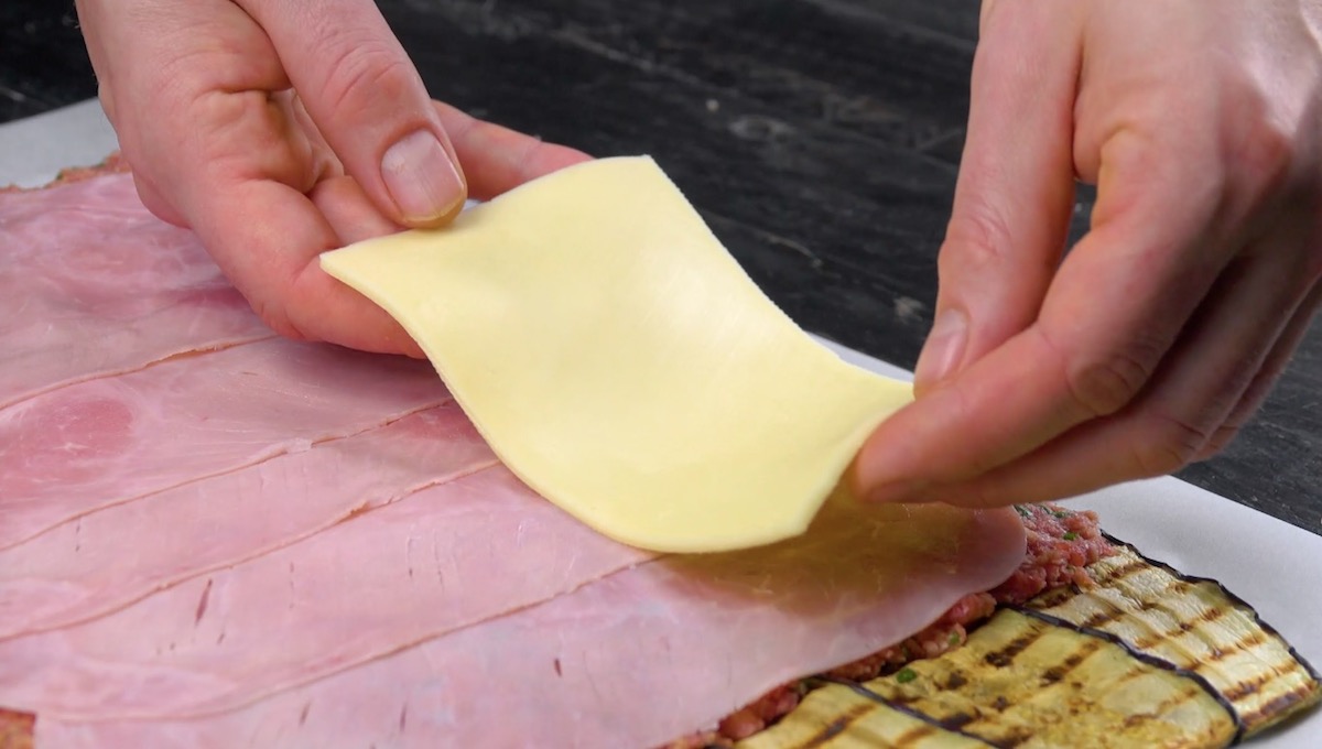 Scheibenkäse wird als letzte Schicht auf Auberginenrolle gelegt