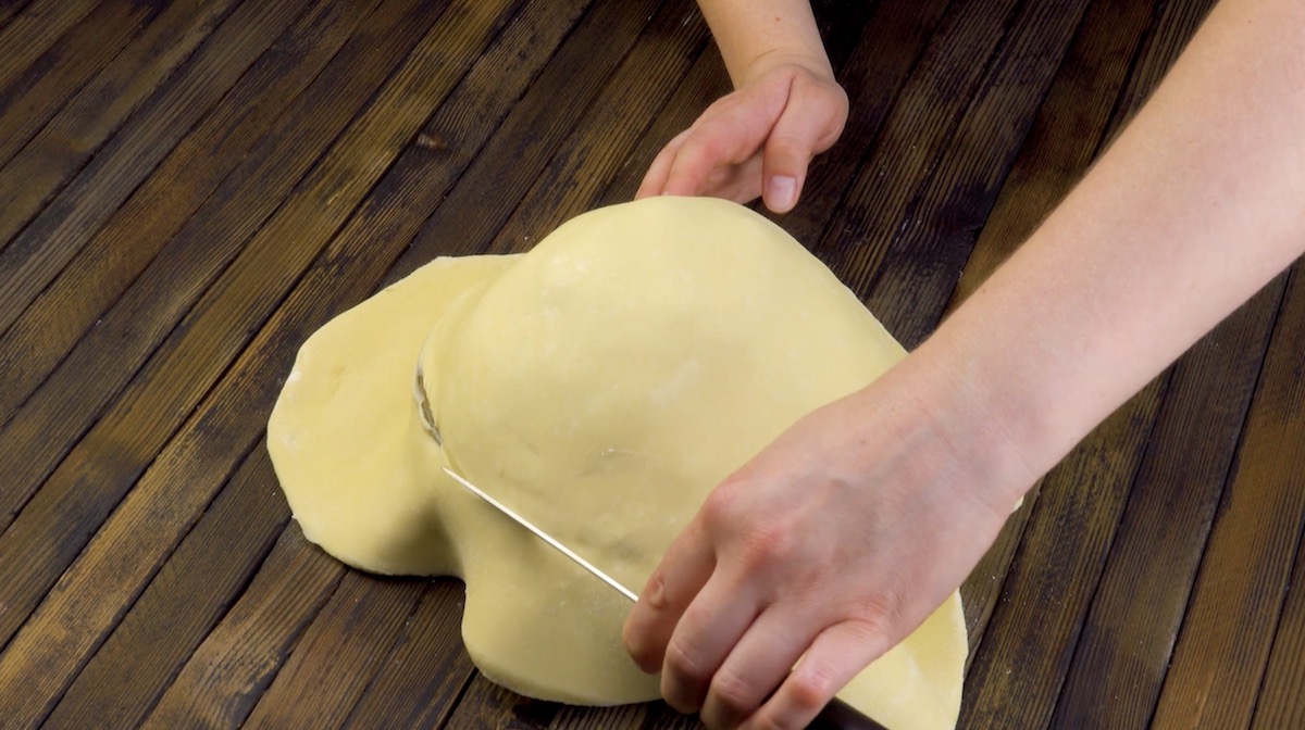 Ausgerollter Teig wird über eine mit Apfelstücken gefüllte Kuchenform gelegt