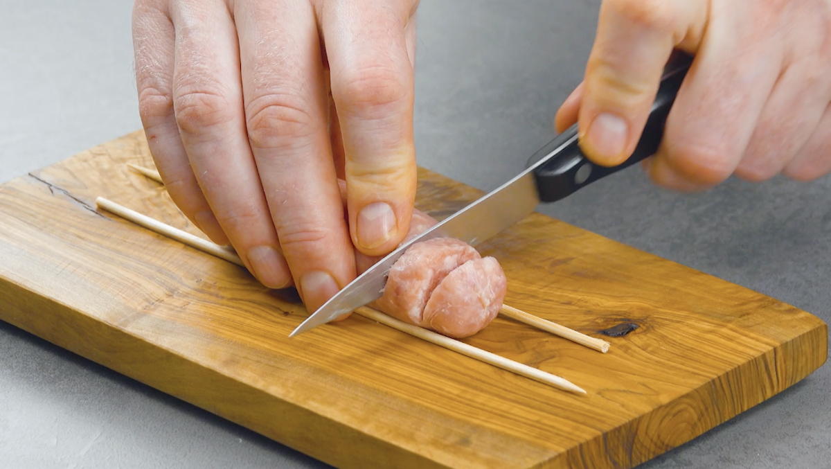 Eine Bratwurst wird zwischen zwei Holzspieße gelegt und eingeschnitten