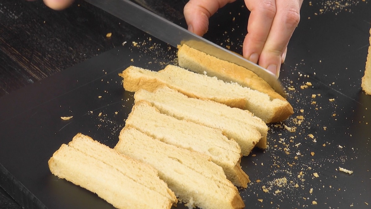 Das Endstück eines Weißbrots wird in Streifen geschnitten