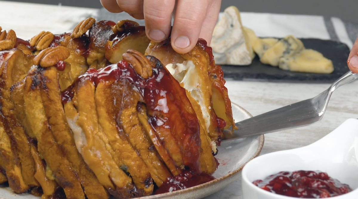 Ein Stück Toastbrotkuchen mit Schweinerücken, Gorgonzola und Birne wird entnommen und mit Pekannüssen und Preiselbeermarmelade serviert