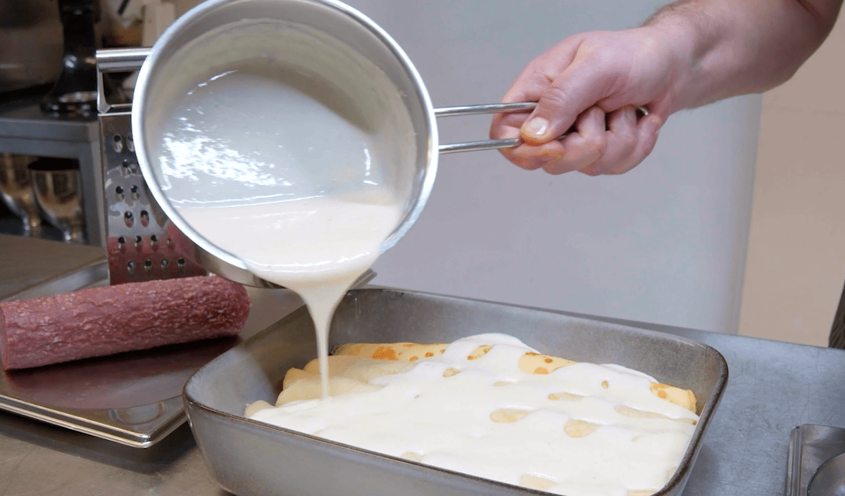 Béchamelsauce wird über die gefüllten Crêpes gegossen