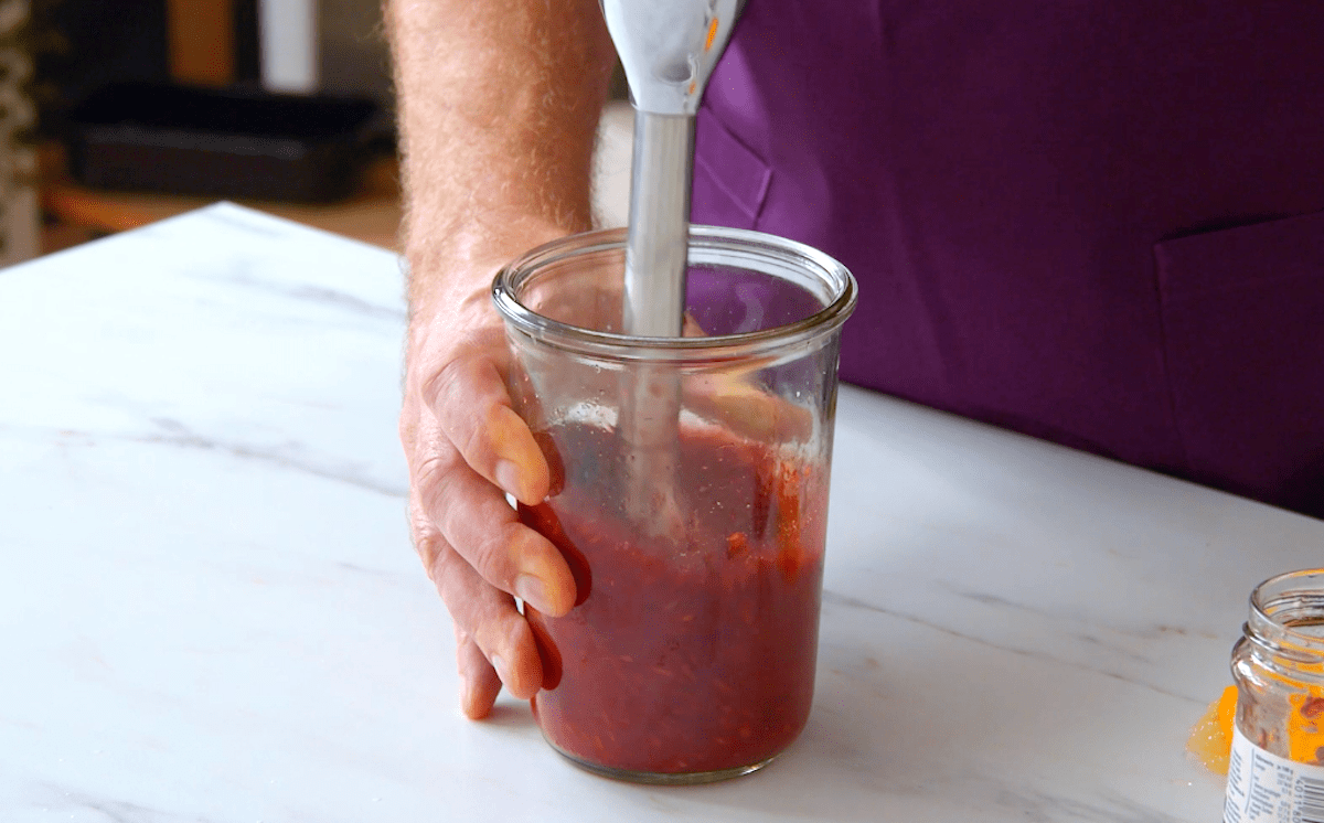 Himbeeren werden in einem hohen Gefäß mit einem Pürierstab püriert
