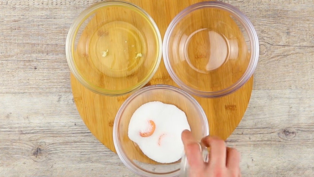 3 Schüsseln auf Holzbrett, von der eine mit Eigelben und Zucker und eine zweite mit Eigelben gefüllt ist