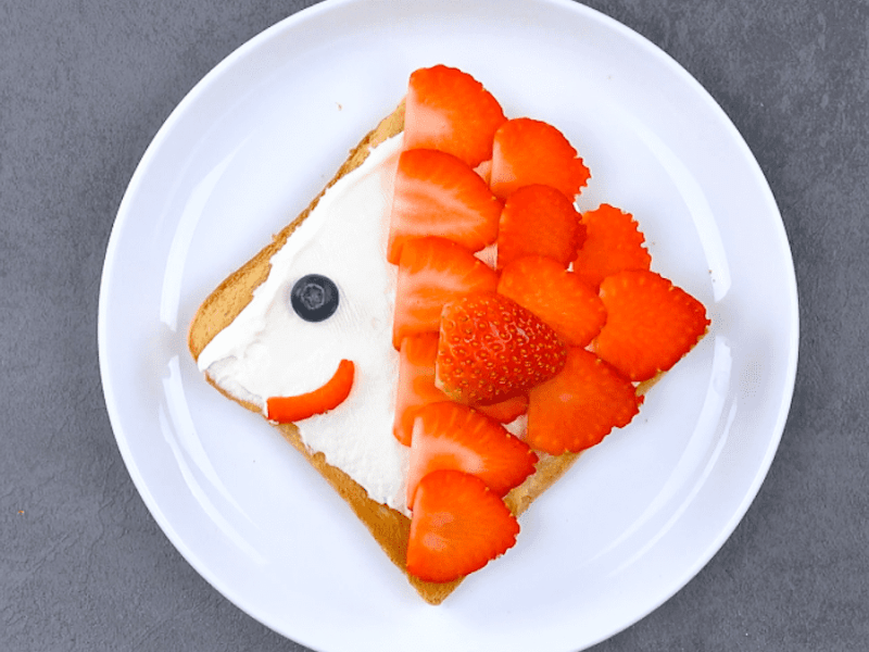 6 Ideen mit Toastbrot: Ein Teller mit einem Toastbrot, das als Fisch dekoriert ist mit Frischkäse und Erdbeerscheiben.