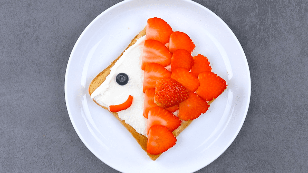 6 Ideen mit Toastbrot: Ein Teller mit einem Toastbrot, das als Fisch dekoriert ist mit Frischkäse und Erdbeerscheiben.