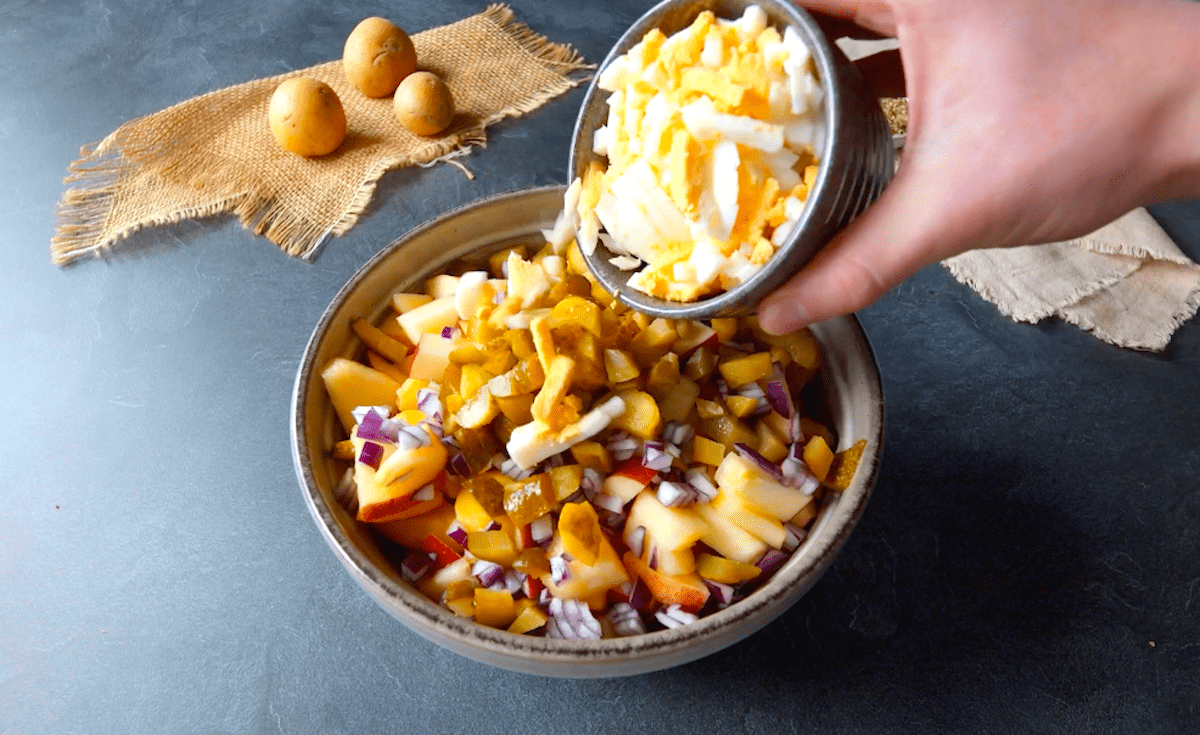 Kleingeschnittene Eier werden in eine Schüssel zu kleingeschnittenen Kartoffeln, Gurken und Zwiebeln hinzugegeben.