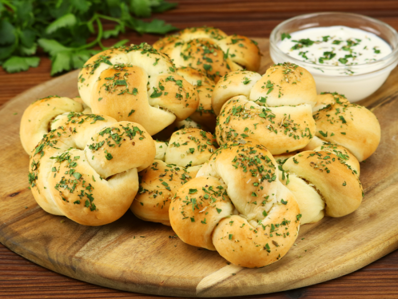 Mehrere Knoblauch-Parmesan-Knoten auf einem runden Holzbrett.