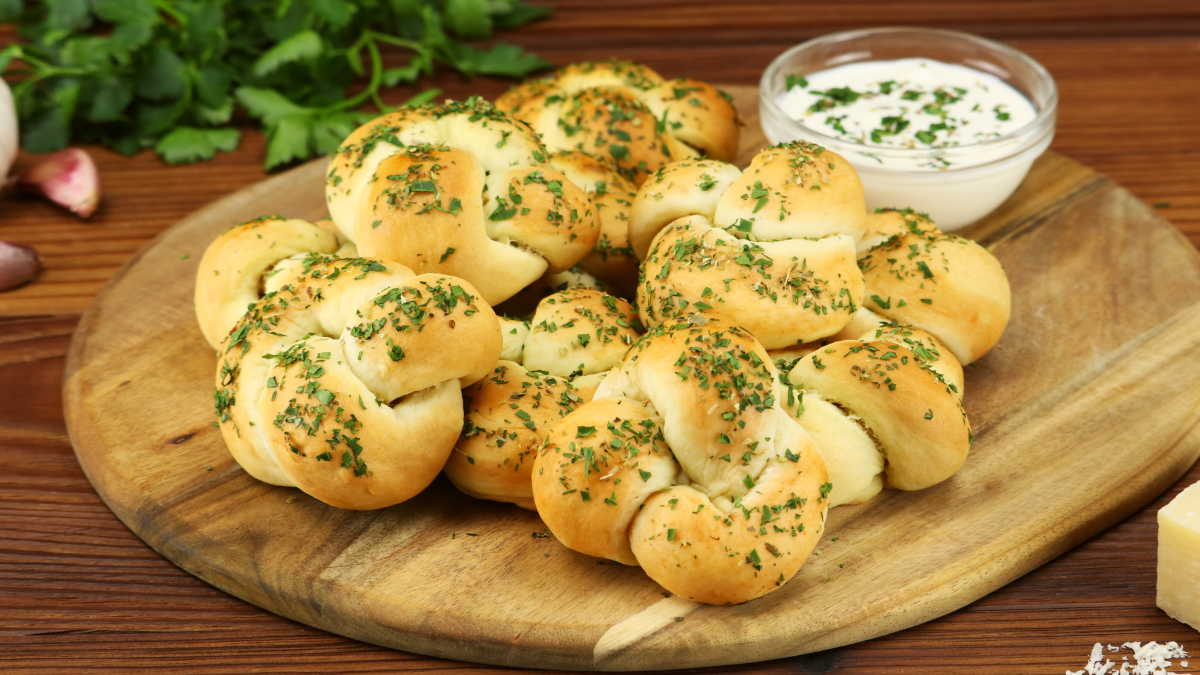 Mehrere Knoblauch-Parmesan-Knoten auf einem runden Holzbrett.
