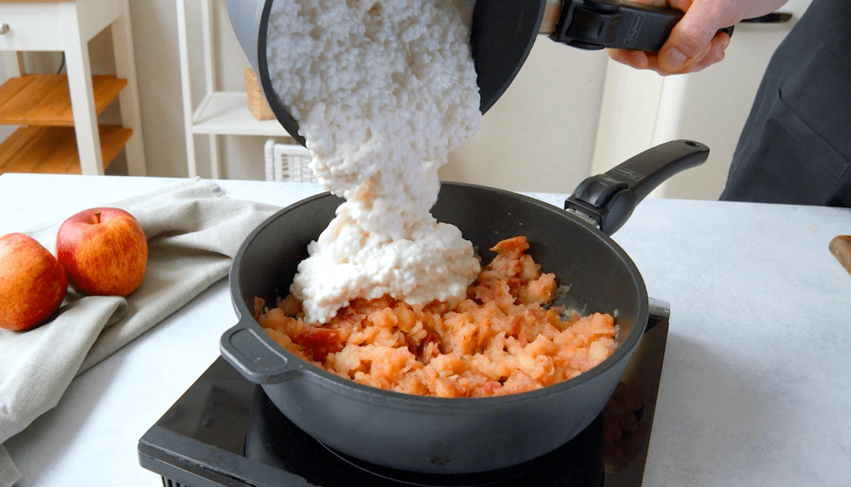 Gekochter Milchreis wird zu zerdrückten Äpfeln in eine Pfanne gegeben