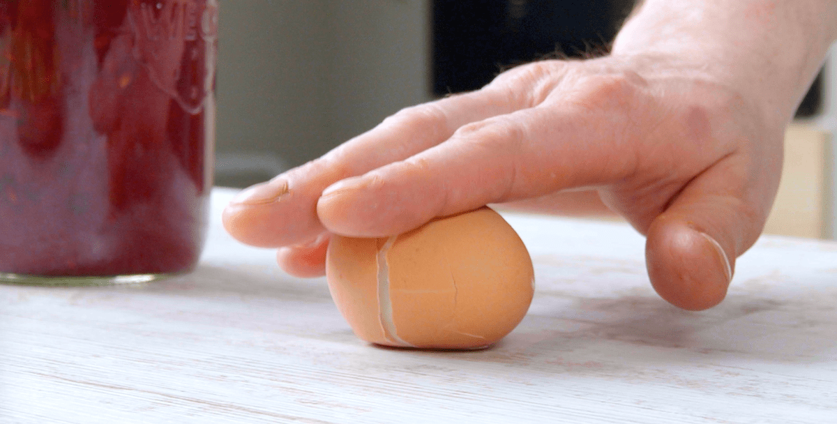 Ein Ei wird über eine Tischplatte gerollt und dabei leicht angedrückt, bis die Schale Risse bekommt.