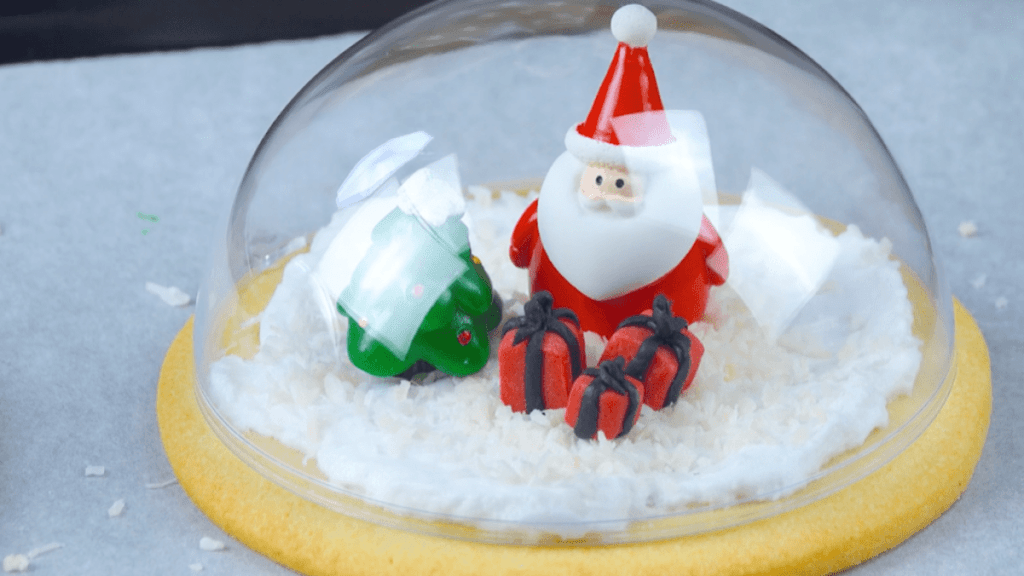 Ein Plätzchen mit essbarer Weihnachtsmann-Figur unter einer Weihnachtskugel-Kuppel.