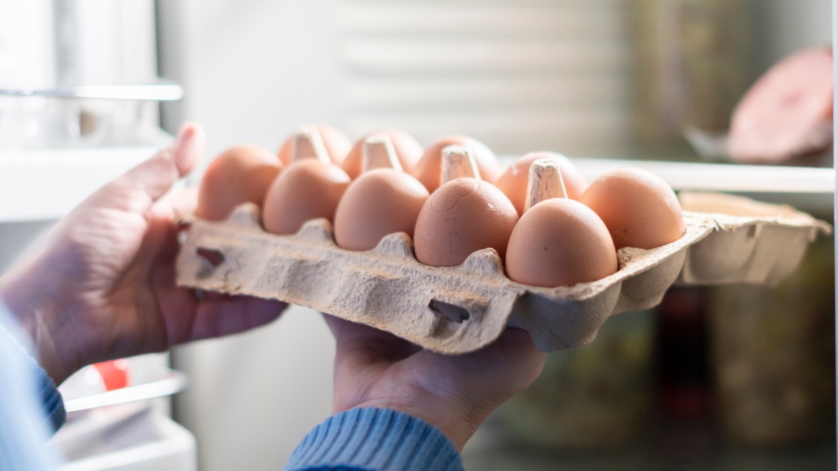 Jemand nimmt eine offene 10er-Packung Eier aus dem Kühlschrank.