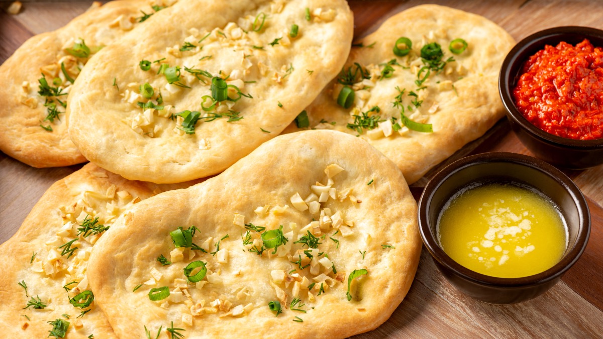 Naan-brote mit Knoblauch neben flüssiger Butter und Dip in kleinen Schüsseln