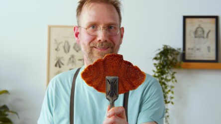 Ein Koch hält einen Croffles mit einer Zange in die Kamera.