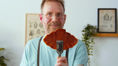 Ein Koch hält einen Croffles mit einer Zange in die Kamera.