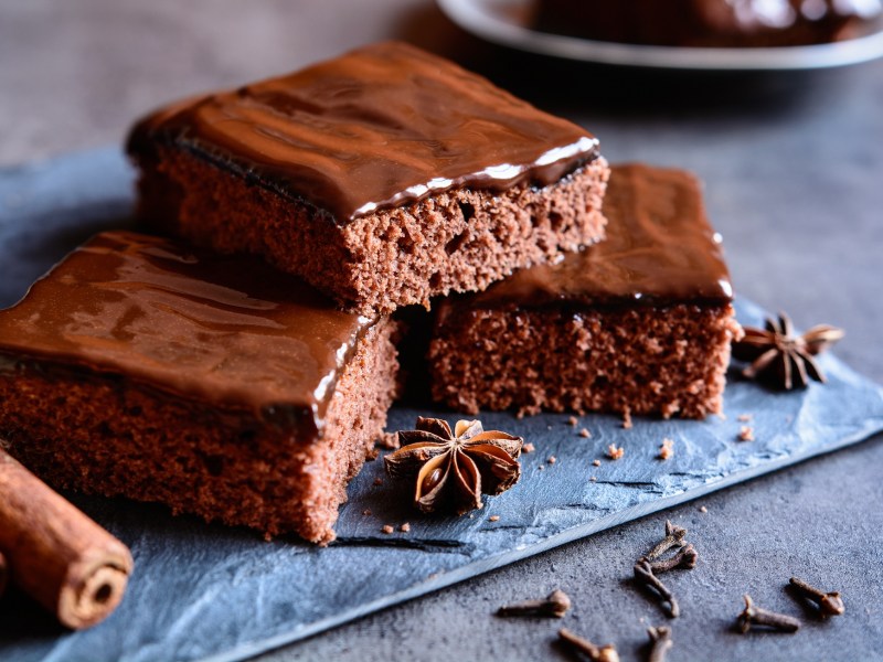 Drei Stücke Gewürzkuchen mit Kuvertüre bestrichen auf einem blauen eckigen Teller.